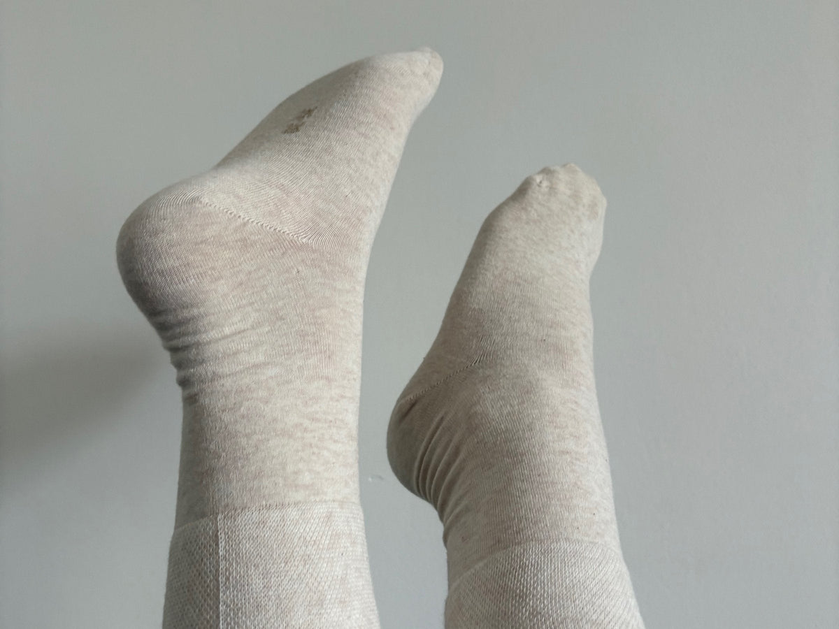Feet in beige Dr. Füss socks, raised against a grey wall